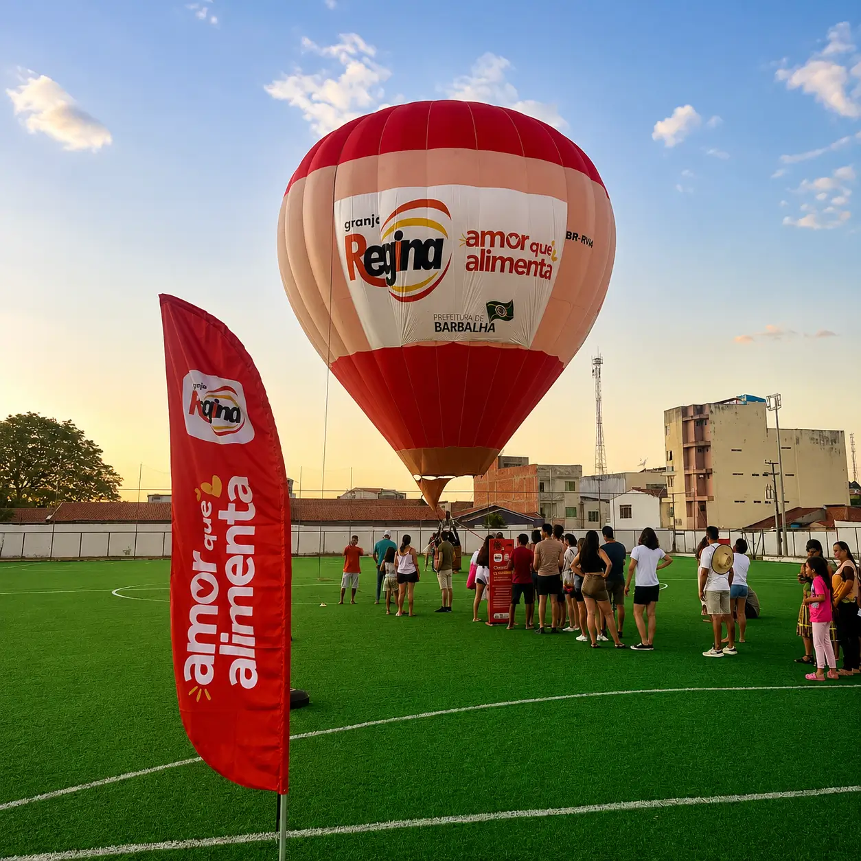 Voo Cativo com Balão Personalizado Granja Regina — Festival e Patrocínio Regional | RVB Balões Balão de ar quente personalizado Granja Regina em voo cativo durante festival regional em Barbalha, com wind banner de apoio em campo de futebol, operação RVB Balões