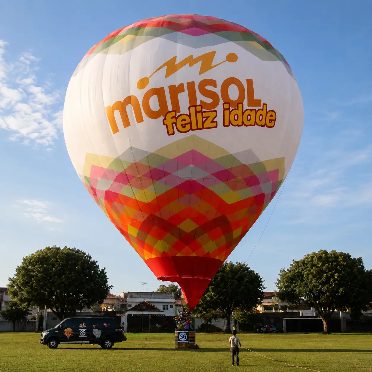 Balão de Ar Quente Personalizado Marisol Feliz Idade — Campanha Corporativa de 35 Anos | RVB Balões Balão de ar quente totalmente personalizado Marisol Feliz Idade com identidade visual colorida e tipografia da marca em campanha corporativa de 35 anos operada pela RVB Balões