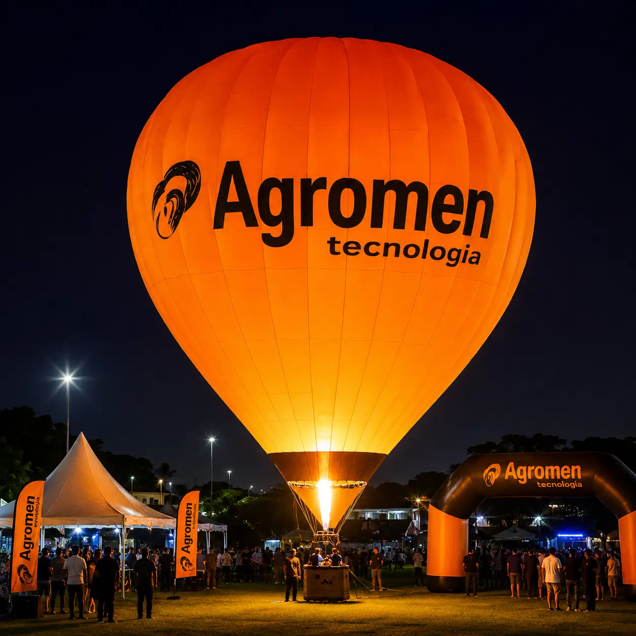 Glow Show com Balão Iluminado Personalizado Agromen Tecnologia — Evento Corporativo Noturno | RVB Balões Balão de ar quente iluminado Agromen Tecnologia em Glow Show, com portal inflável de entrada e wind banners em evento corporativo noturno operado pela RVB Balões