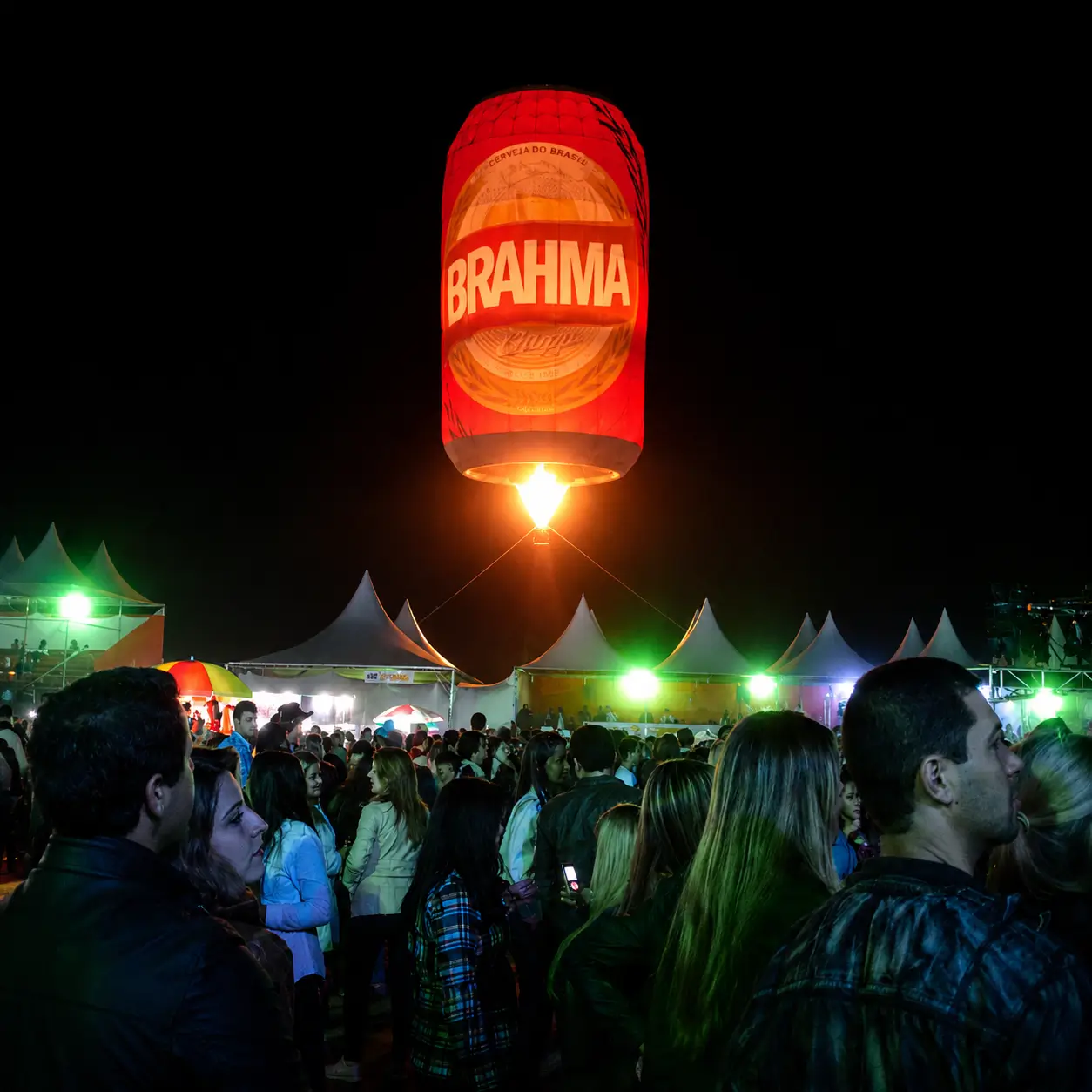 Glow Show com Balão Iluminado Special Shape Brahma — Formato de Lata em Festival Noturno | RVB Balões Balão iluminado Special Shape Brahma em formato de lata de cerveja sobre festival noturno operado pela RVB Balões em Glow Show
