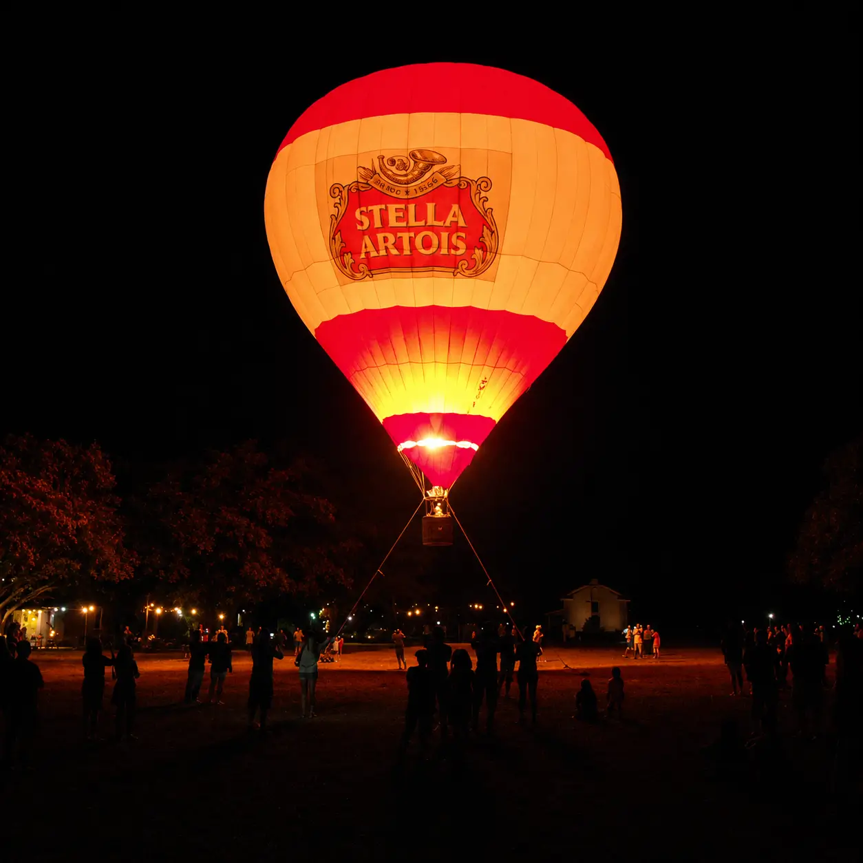 Glow Show com Balão Iluminado Personalizado Stella Artois — Espetáculo Noturno de Aeromarketing | RVB Balões Balão de ar quente iluminado Stella Artois em Glow Show noturno operado pela RVB Balões durante ativação de marca