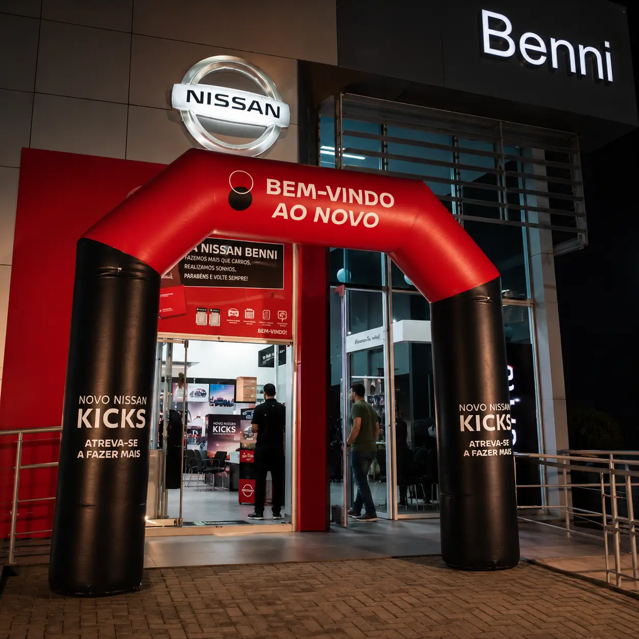 Portal inflável personalizado da Nissan instalado na entrada de concessionária durante evento automotivo noturno de lançamento e recepção de clientes.