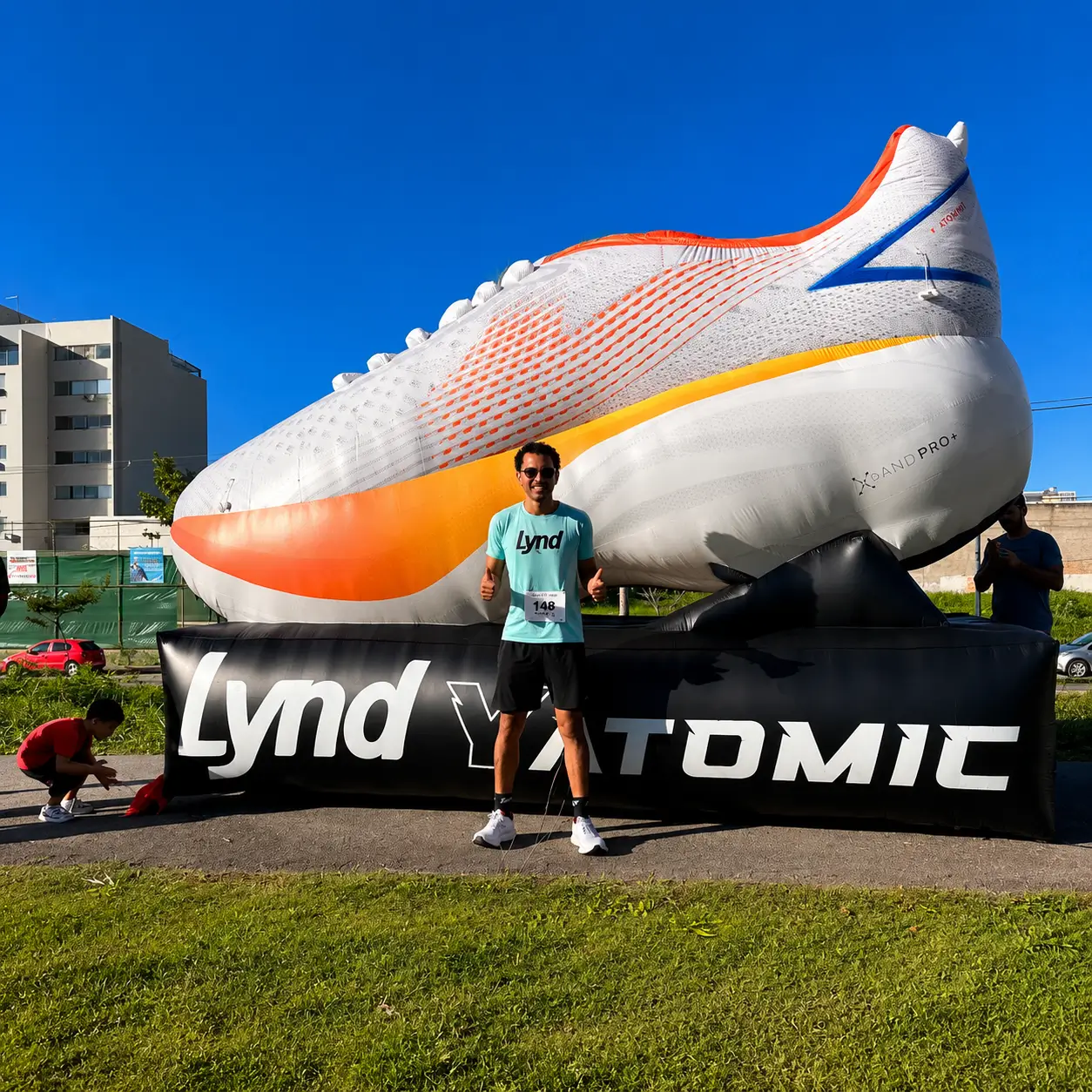 Réplica inflável personalizada de tênis gigante da Lynd em evento promocional ao ar livre com cliente posando ao lado da estrutura inflável.