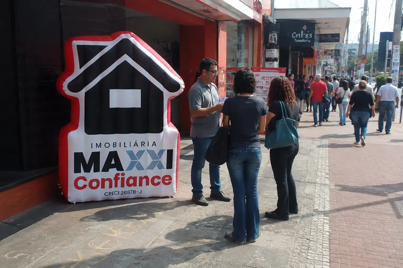 PDV itinerante de imobiliária com inflável promocional em formato de casa instalado em área comercial de grande circulação para atrair clientes.