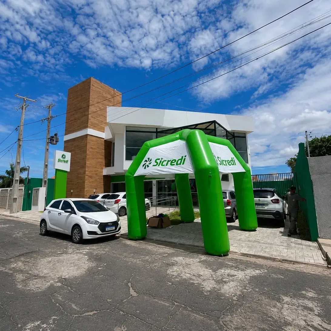 Tenda inflável personalizada Sicredi verde 4x4m instalada na fachada de agência cooperativa em dia de inauguração, fabricada pela RVB Balões